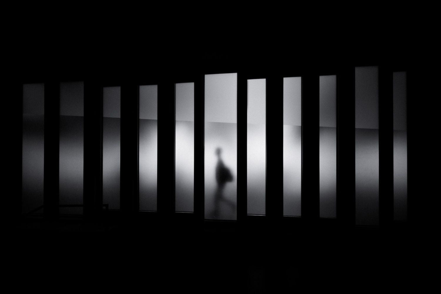 rhythmic photo of man walking behind windows