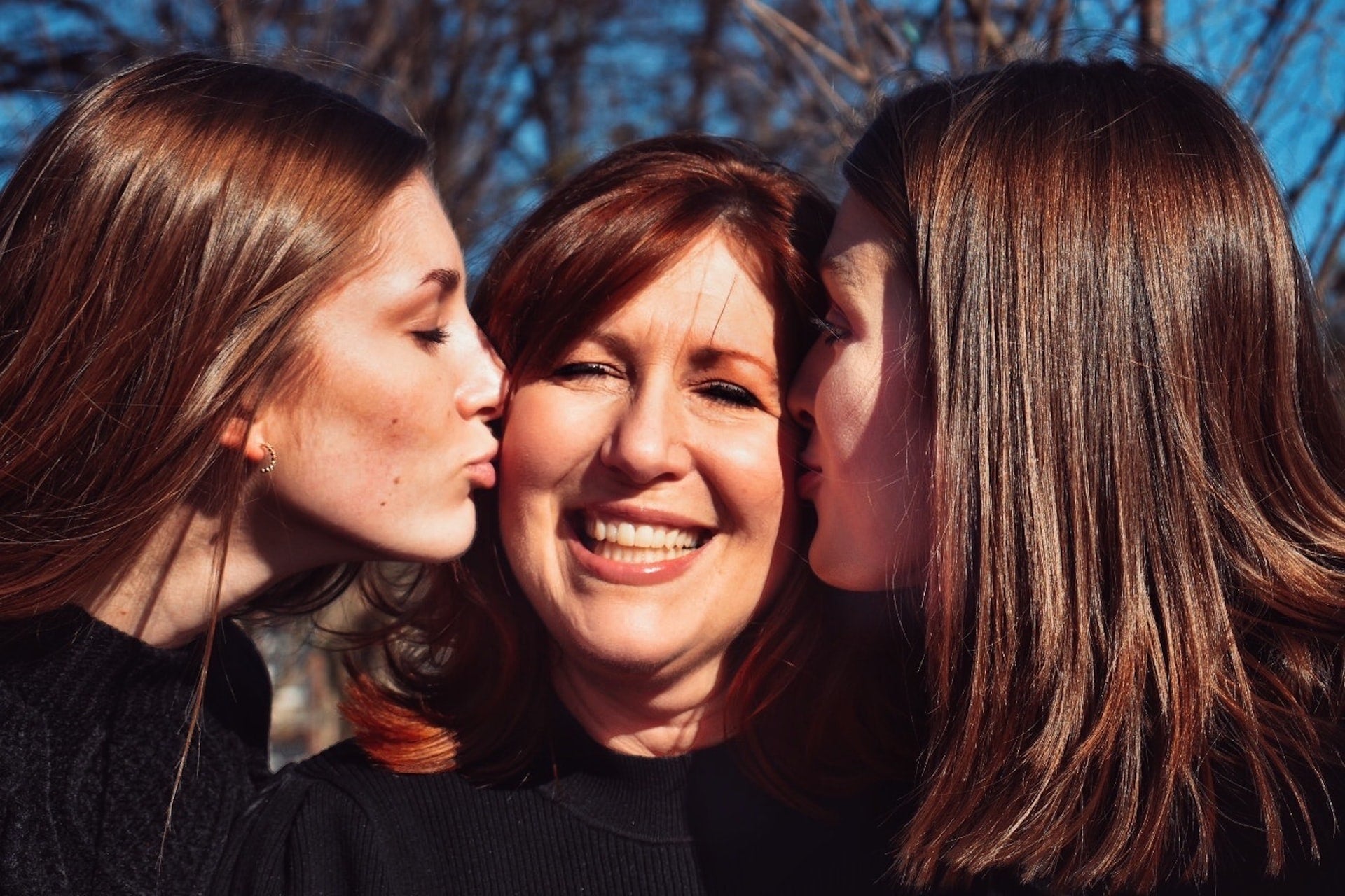 a mum is kissed by her two daughers on each cheek