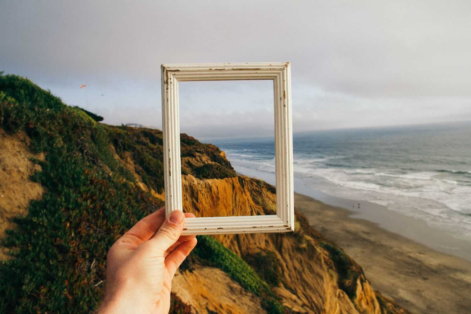 hand holding a photo frame by the sea and stones Photo by Pine Watt on unsplash