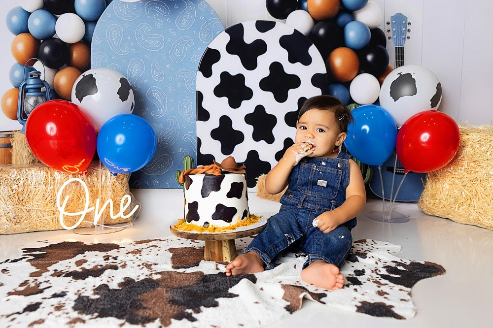 Baby boy eating cake in front of a cow-boy themed cake smash photo set.