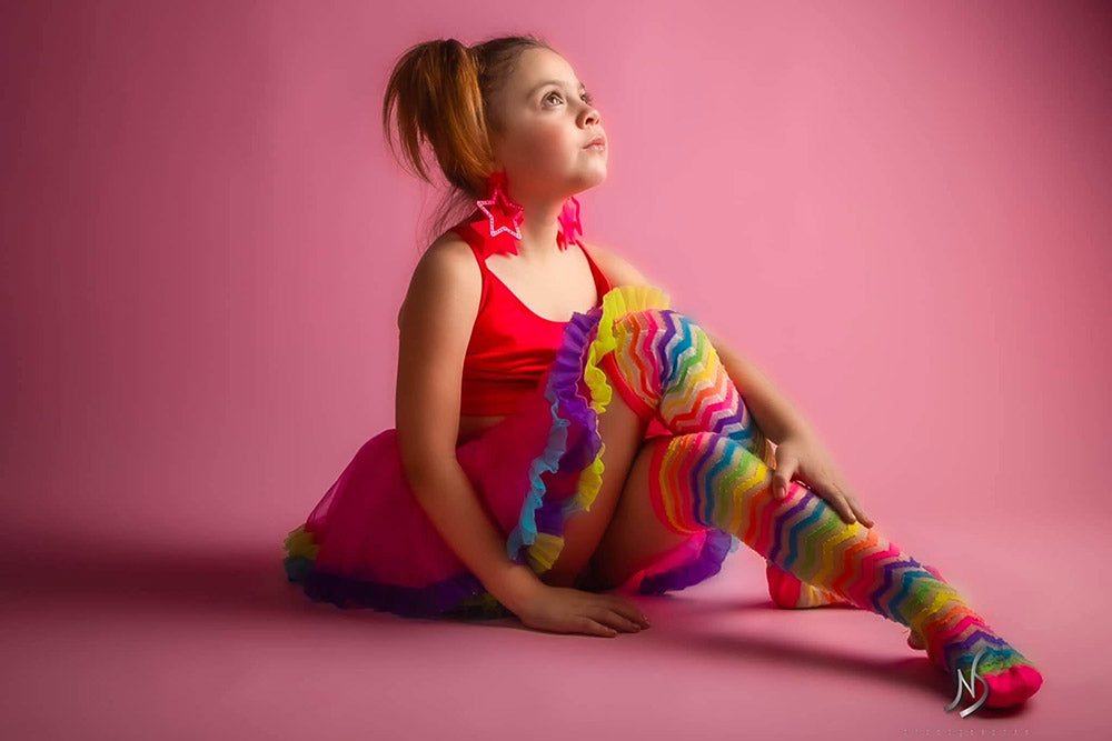 A girl wearing colorful clothes is taking photos with a pink background