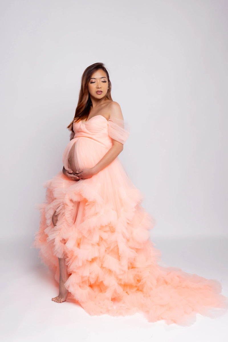 Pregnant woman standing sideways in pink lace maternity dress for a photo shoot