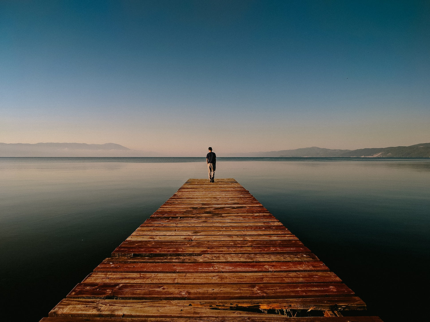 man standing on the edge of the pier over lake background Photo by Adib Harith Fadzilah on Unsplash
