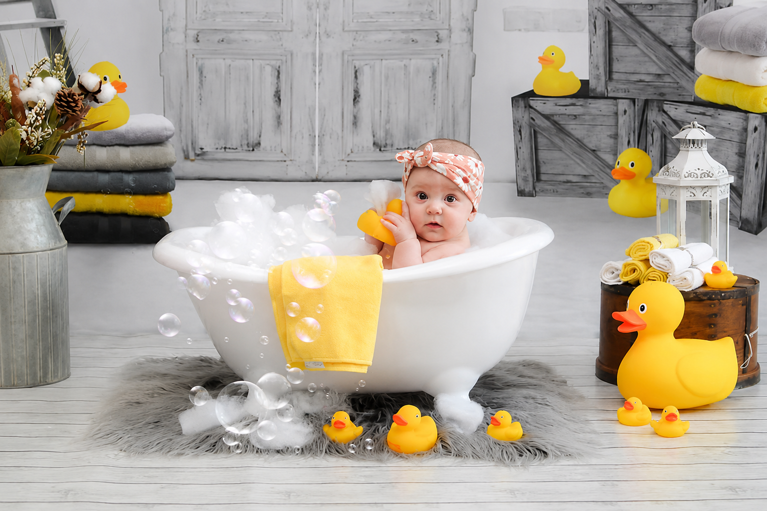 Baby sitting in a white tub for a bright summer portrait scene with rubber ducks, bubbles, soft towels, and rustic studio details.